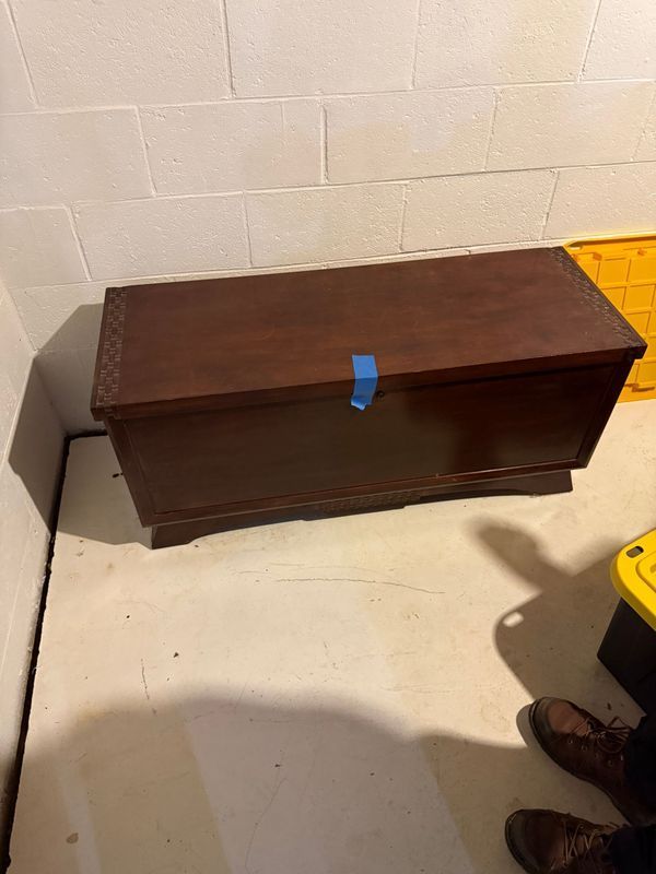 Brown wooden chest against a white-brick wall in a basement.