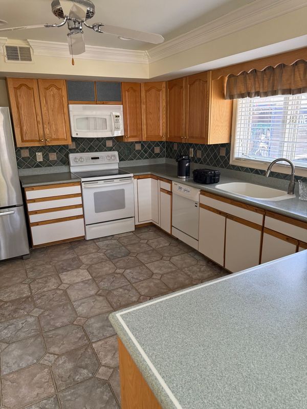 Kitchen with wooden cabinets, white appliances, gray countertops, and tiled floor.
