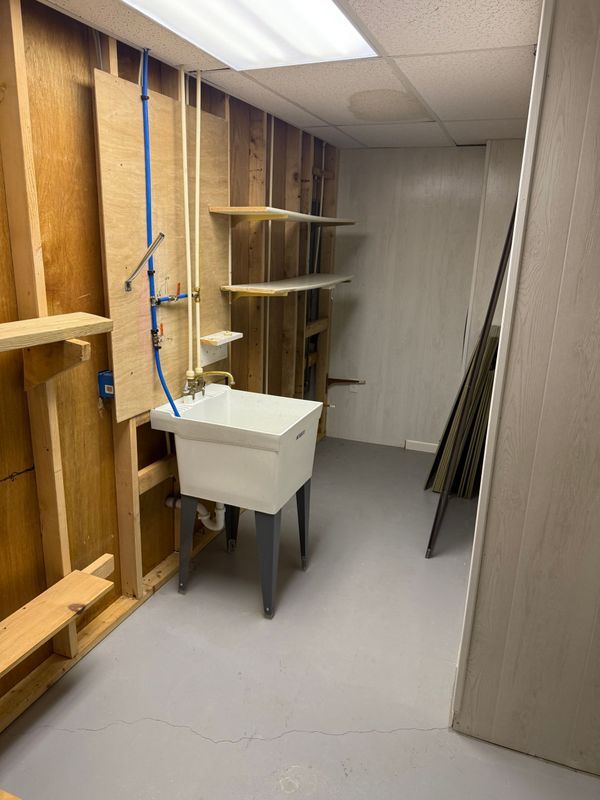 A utility room with a utility sink, wooden shelving, and bare walls. Gray floor.