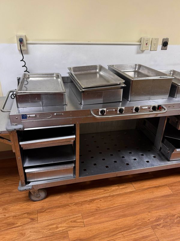 Stainless steel food cart with trays and drawers.