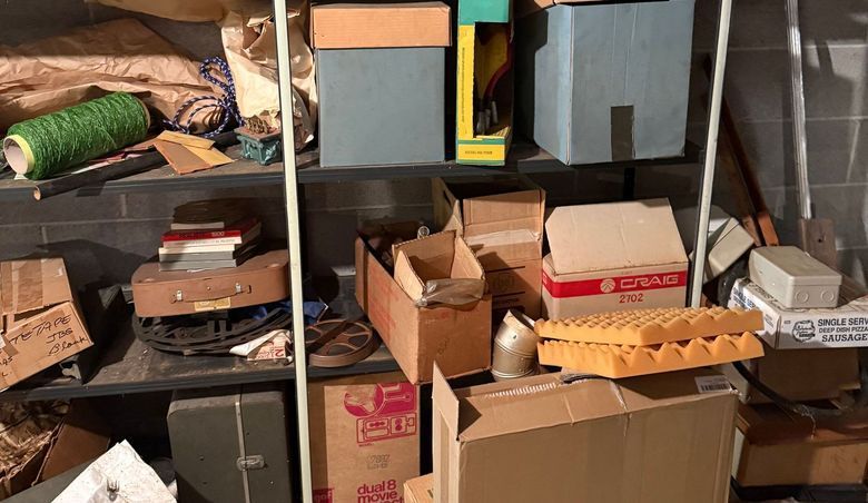 Cluttered shelves in a storage area. Boxes, spools, and various items are haphazardly arranged.