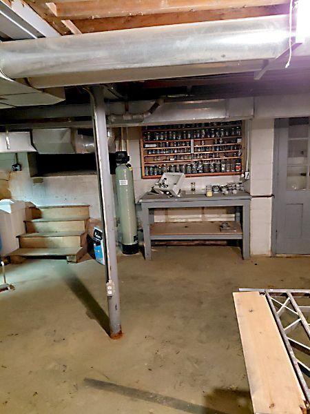 Basement workspace with workbench, support beam, water softener, and stairs.
