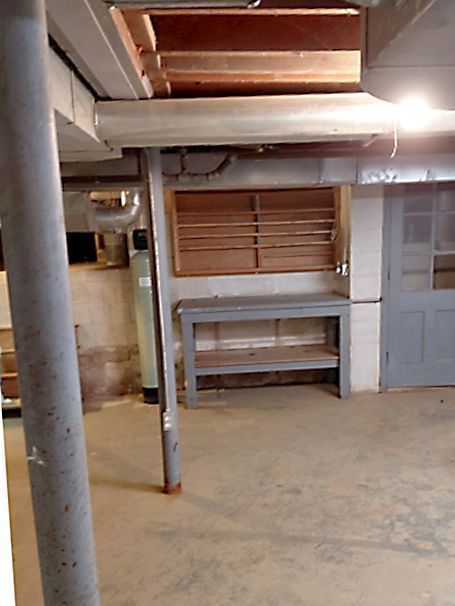 Basement with a workbench, wooden rack, and support beam. Concrete floor and walls.