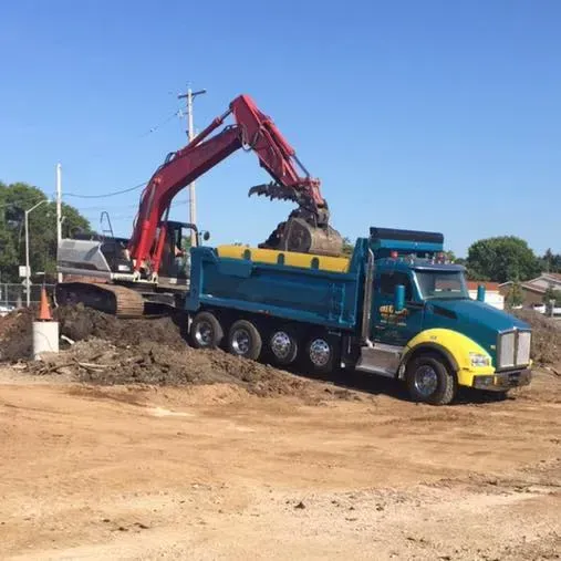 Excavator loading dirt into a turquoise dump truck on a construction site under a clear blue sky.