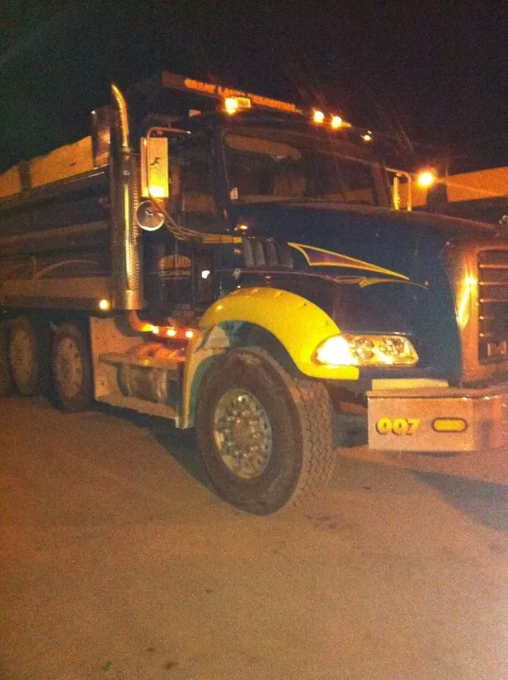 Dark blue dump truck with yellow accents on a dark road at night.