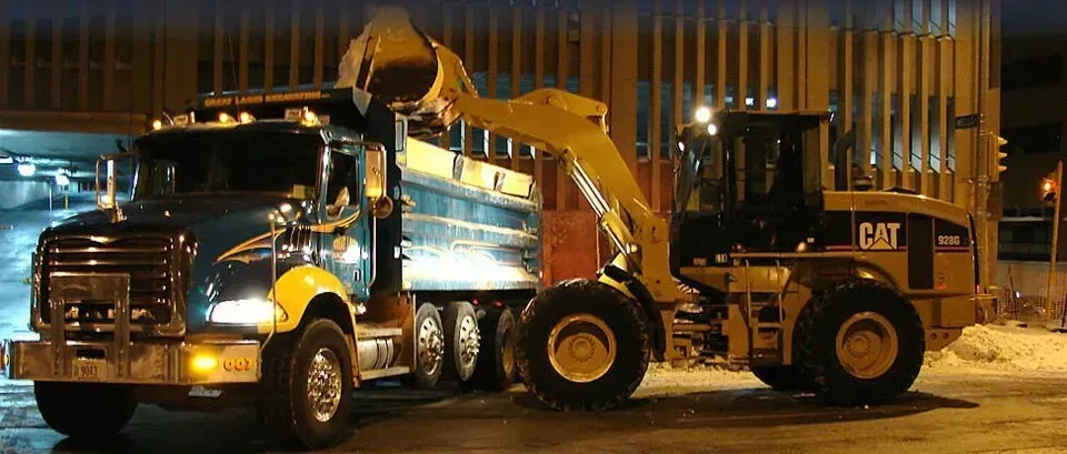 A blue dump truck is being loaded by a yellow Caterpillar loader. They are under a building at night.