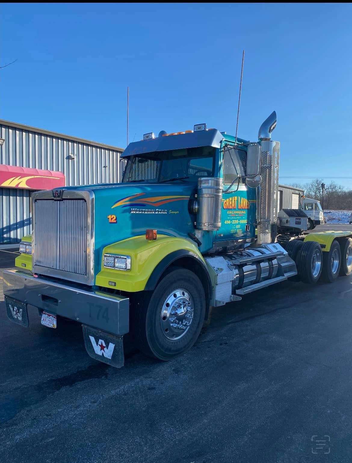 Teal and yellow Western Star semi-truck parked in front of a building on a sunny day.