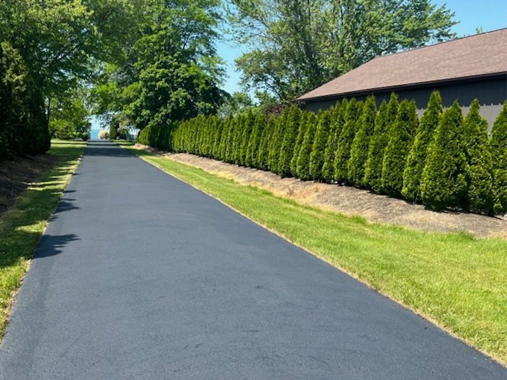 a driveway with a house in the background and a lot of trees on the side of it.