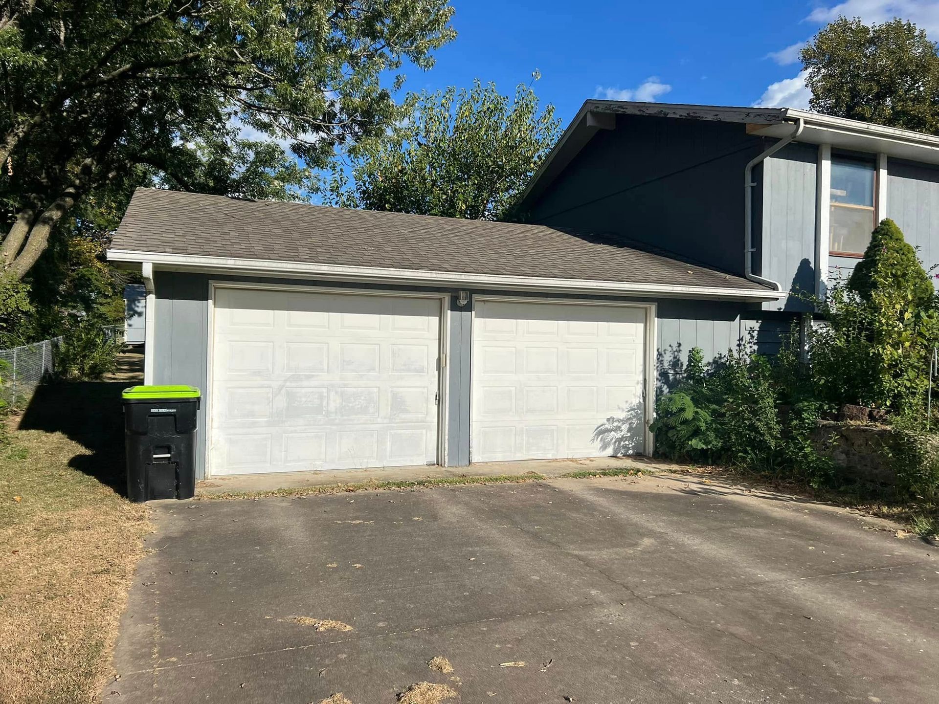 A house with a garage and a trash can in front of it