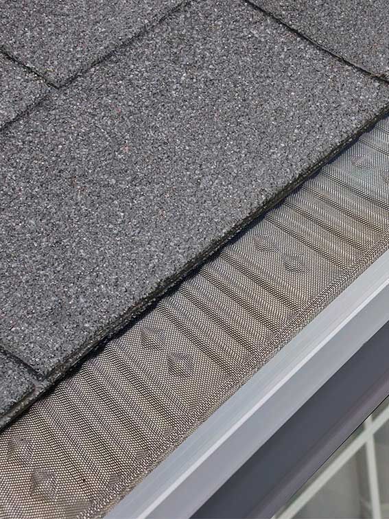 A close up of a gutter on a roof with shingles.