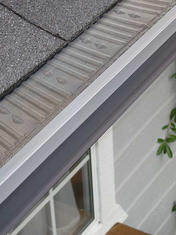 A close up of a gutter on a roof next to a window.