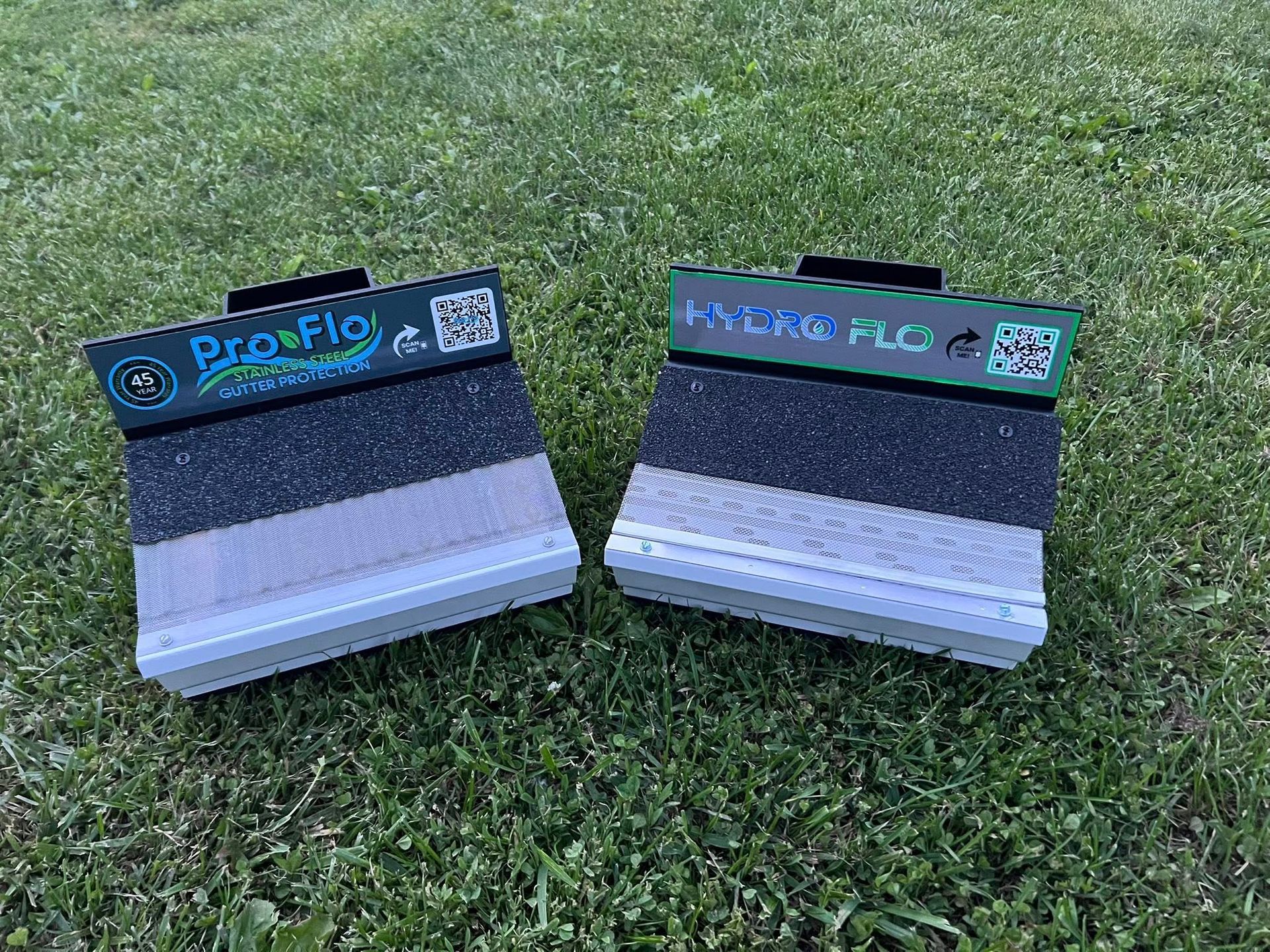 Two boxes are sitting on top of a lush green field. Gutter guards hydro flo and pro flo brand gutters guards.