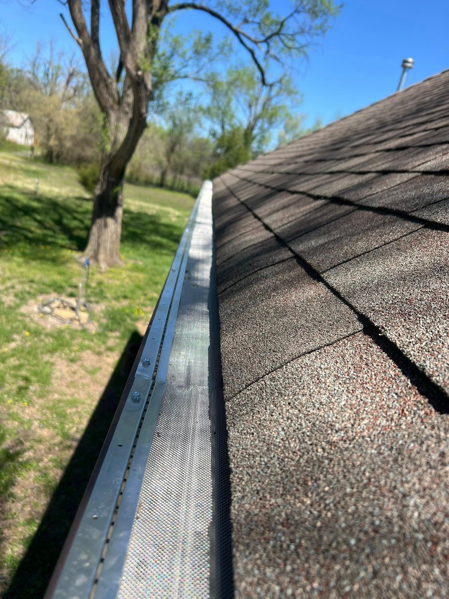 A close up of a gutter on a roof with a tree in the background.