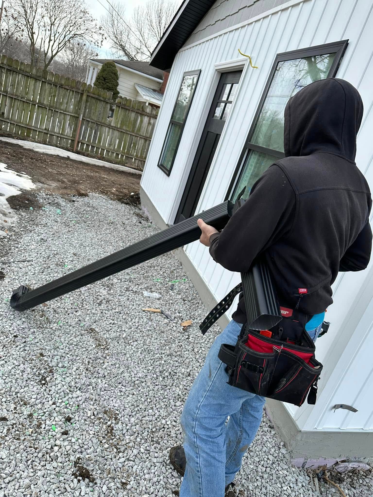 A man in a hoodie is carrying a large piece of metal in front of a house.