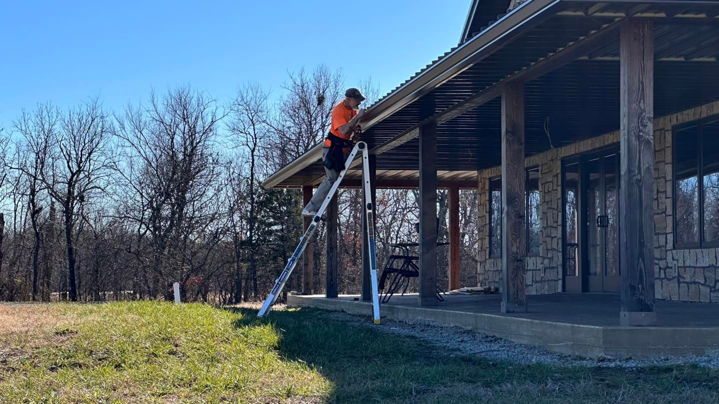 A man is standing on a ladder working on the roof of a house.
