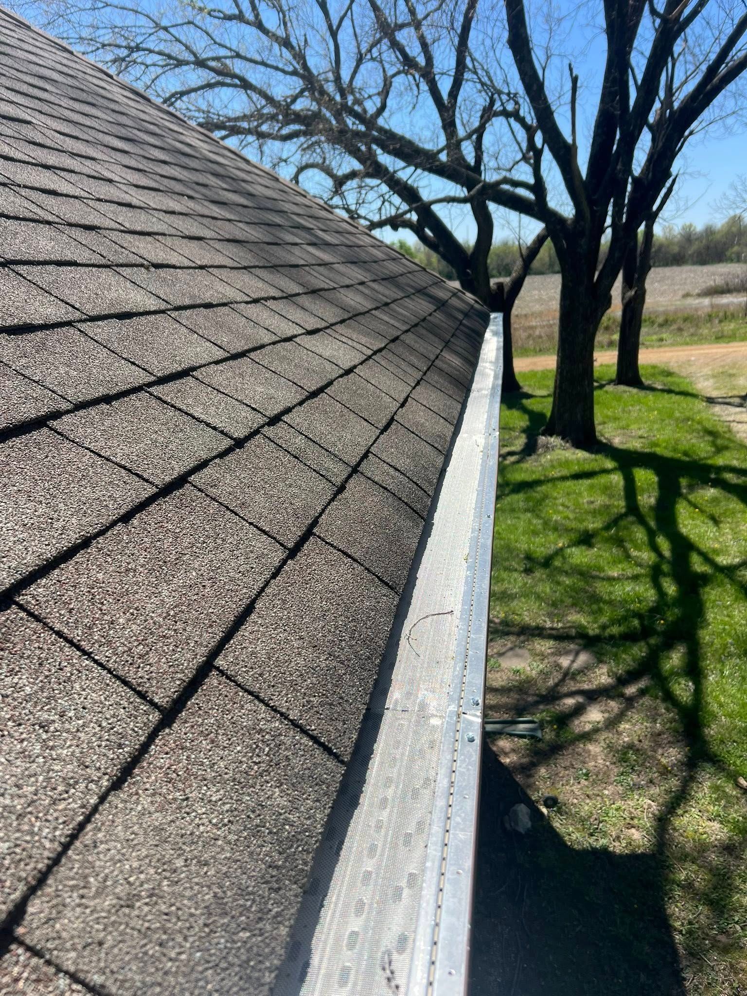 A close up of a gutter on a roof with trees in the background.