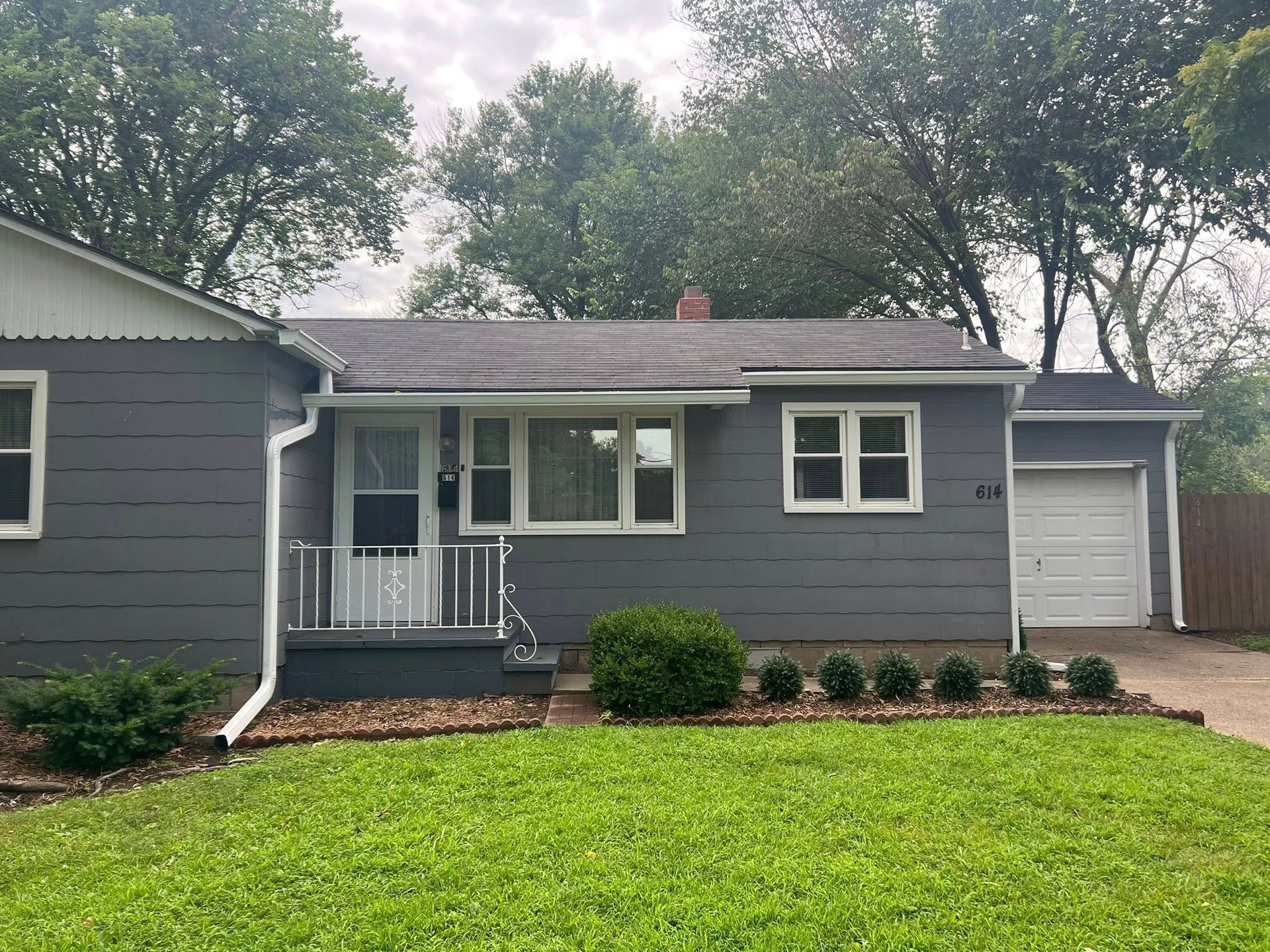 A small gray house with a large lawn in front of it.