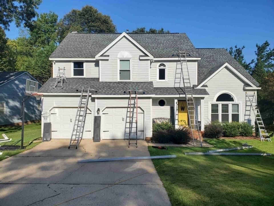 A large white house with a gray roof is being painted.