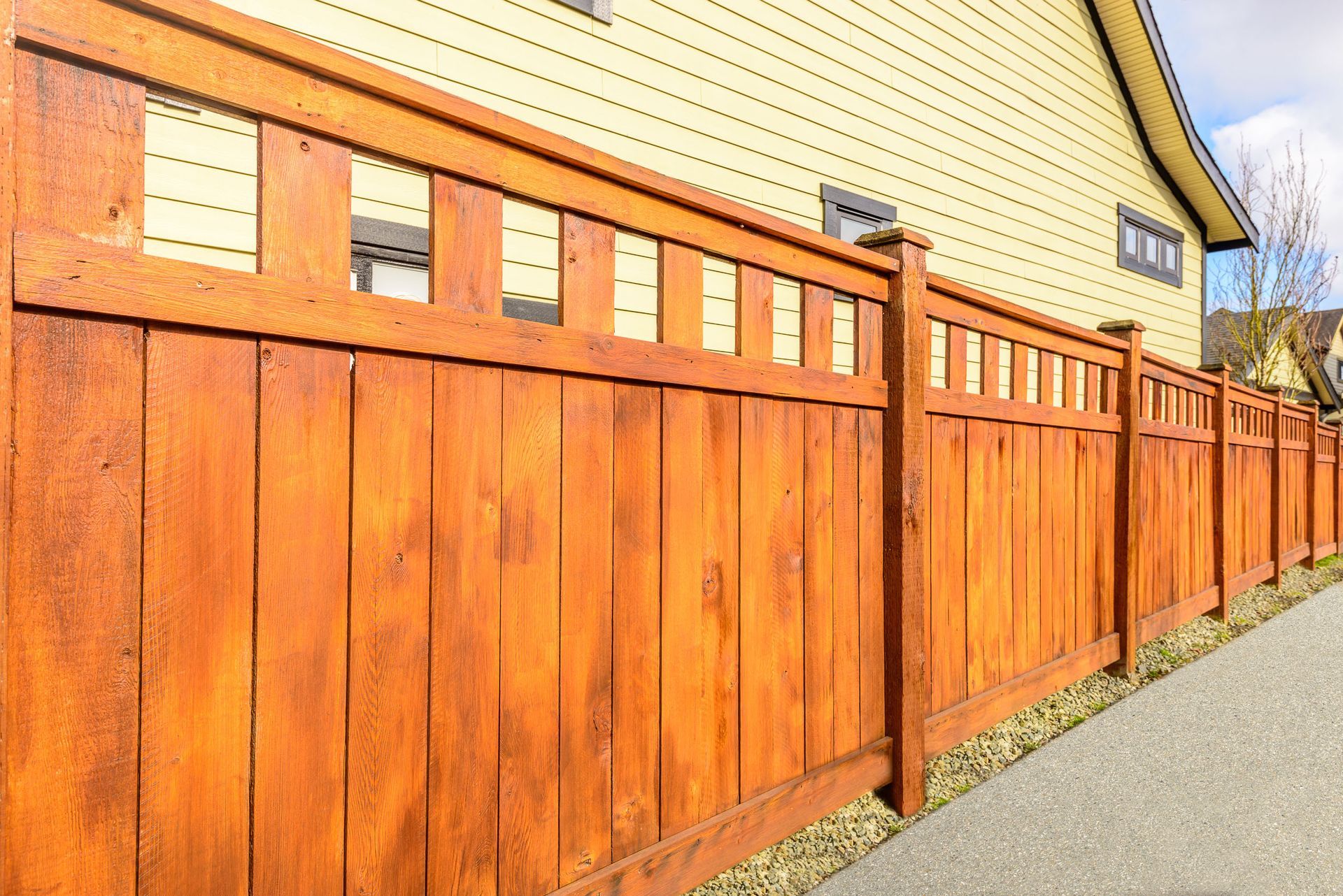 A wooden fence along a sidewalk in front of a house.