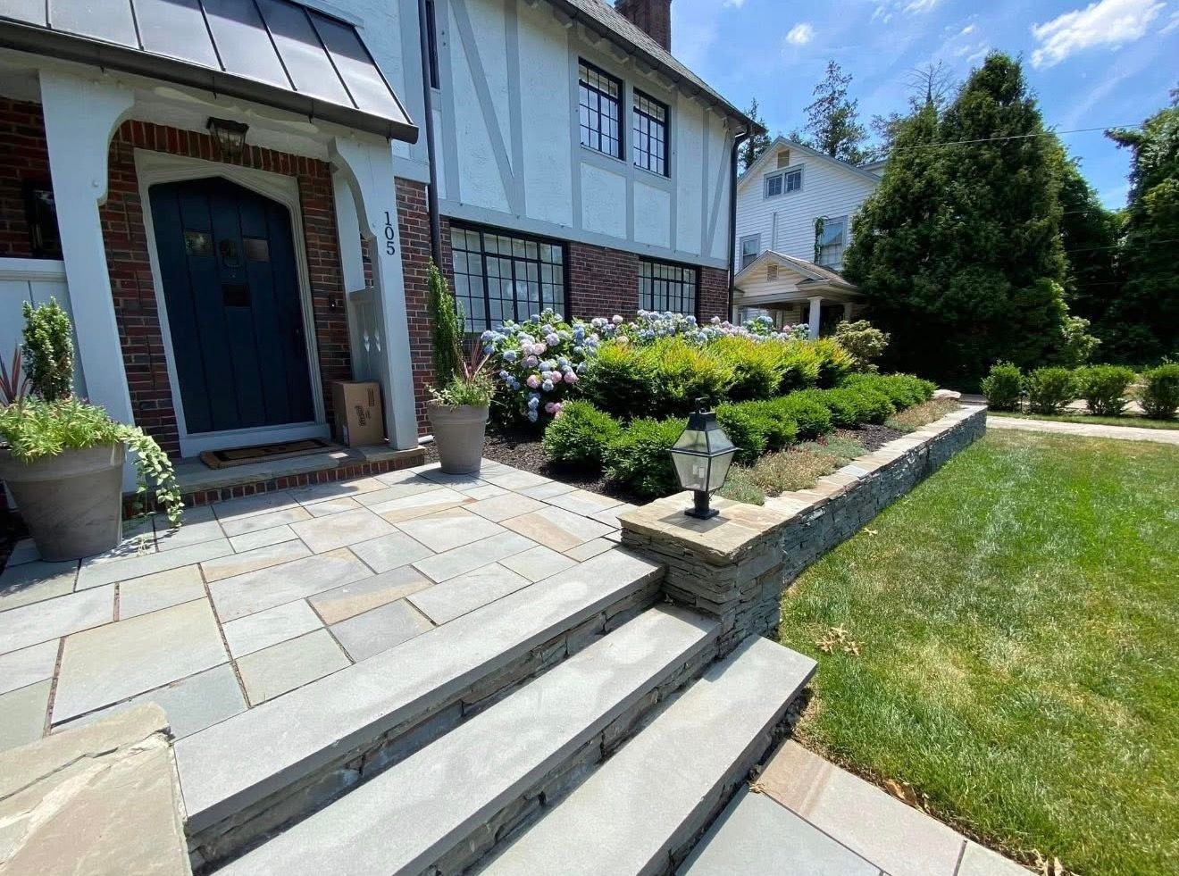 Stone steps lead to the entrance of a Tudor-style home with a front garden and a stone retaining wall.