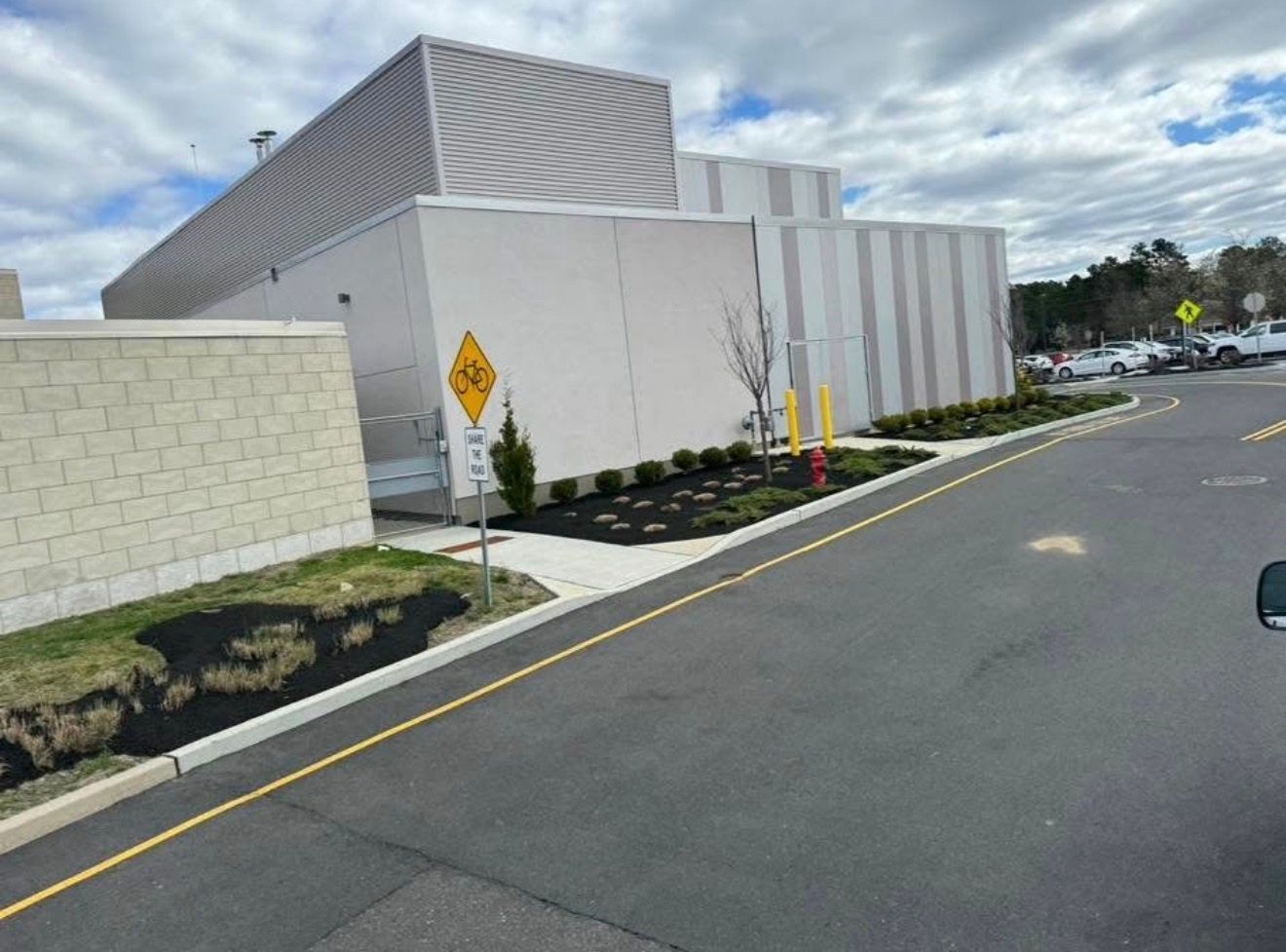 A side view of a modern, multi-textured beige commercial building with a parking lot and a pedestrian crossing sign.