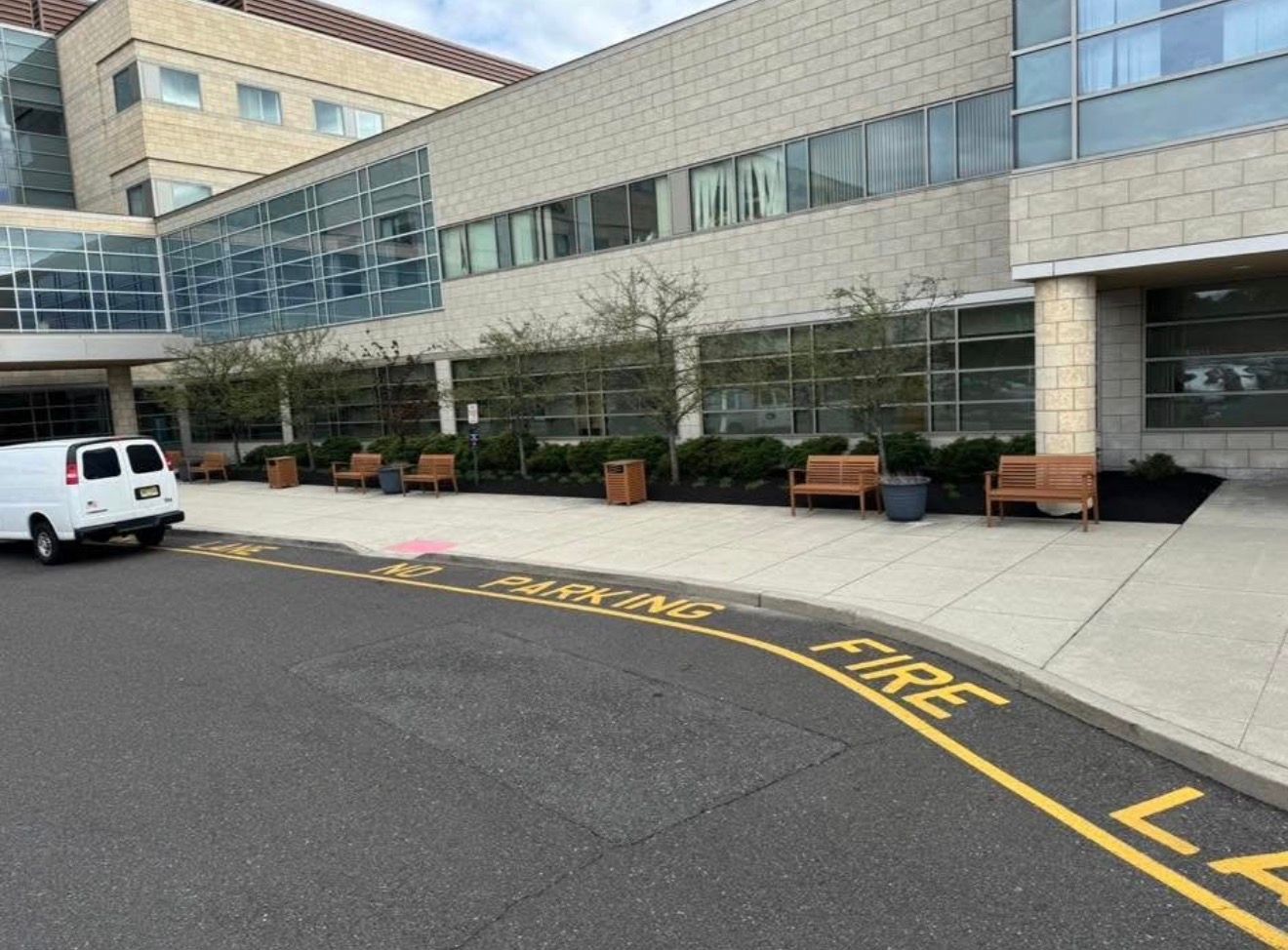 A white van parked outside a modern building with a paved walkway, benches, and 