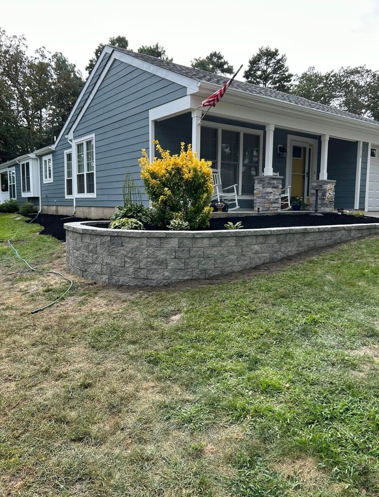 A blue house with a covered porch and stone retaining wall in the front yard.