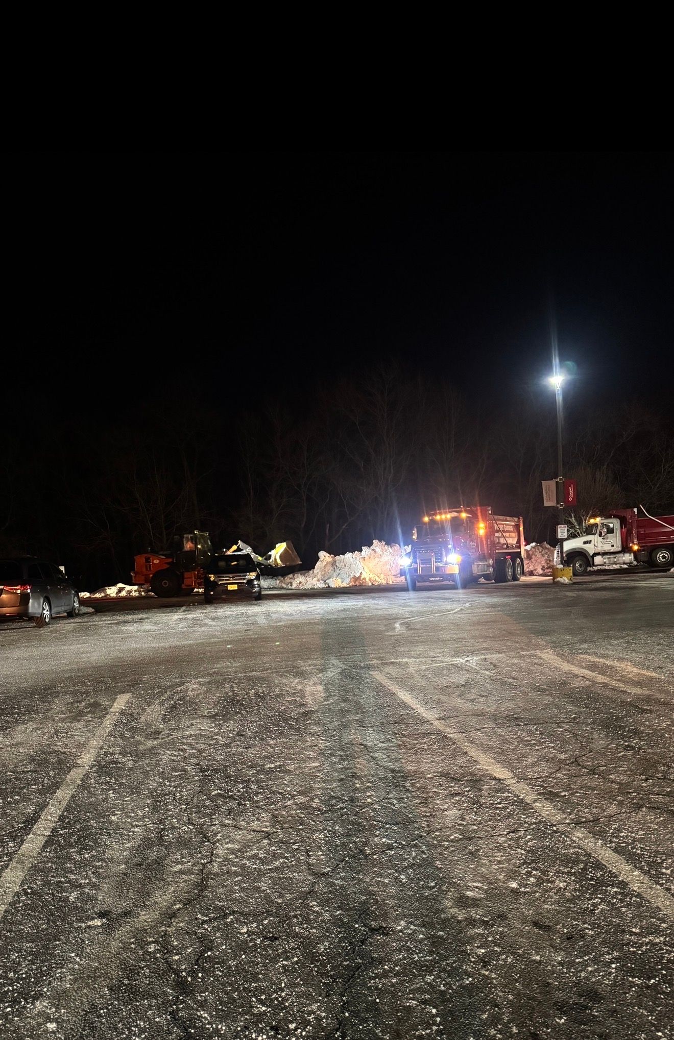 A night view of emergency vehicles with flashing lights on a gravel lot covered in a light dusting of snow.