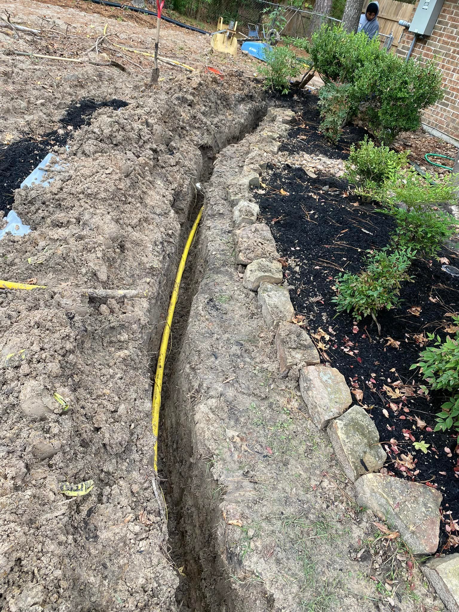 A yellow hose is laying in the dirt next to a stone wall.
