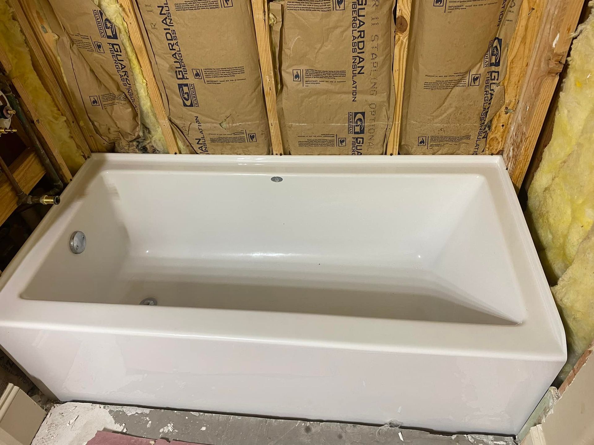 A white bathtub is sitting in a bathroom next to a wall with insulation.