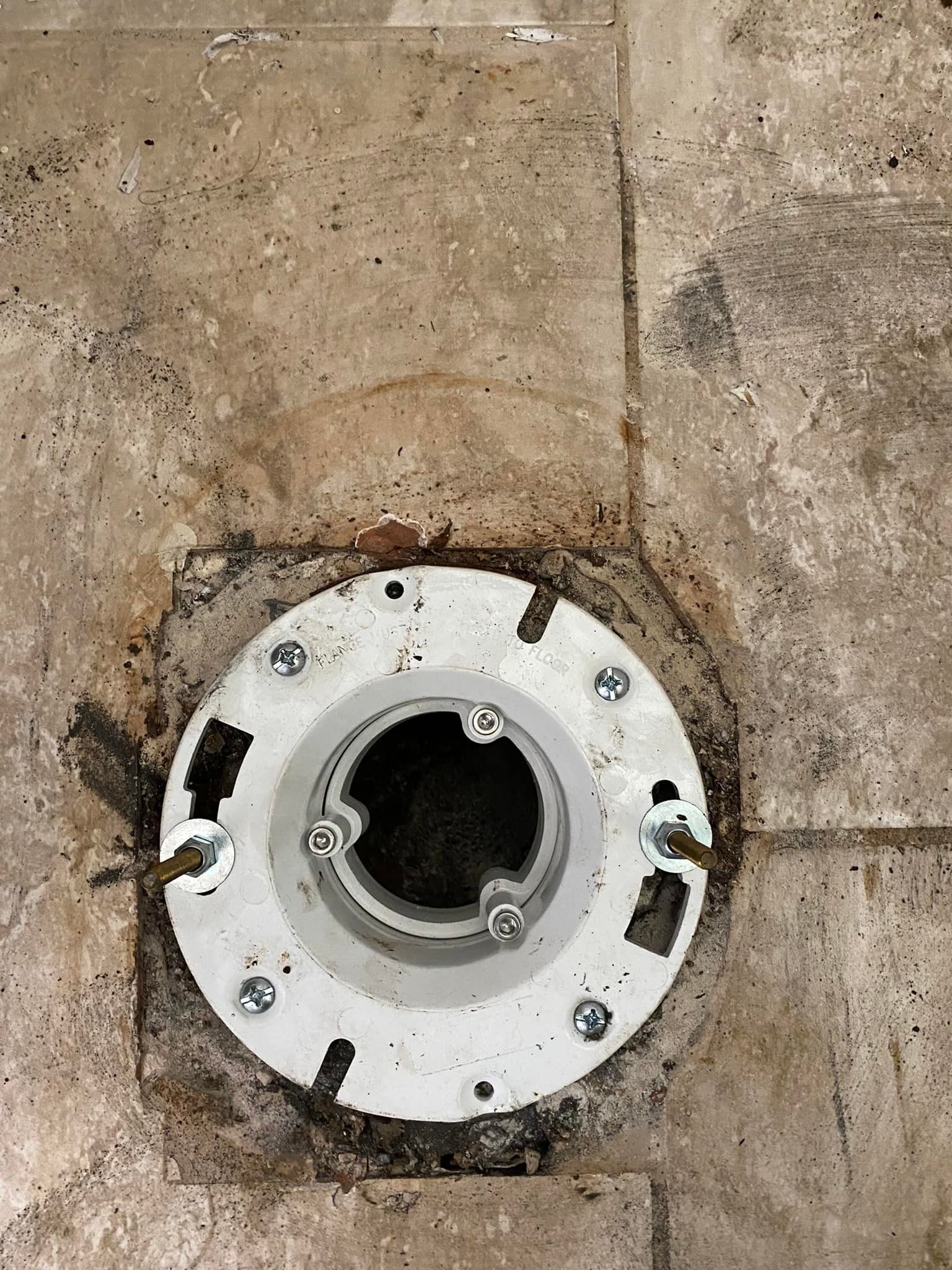 A close up of a toilet flange on a tiled floor.