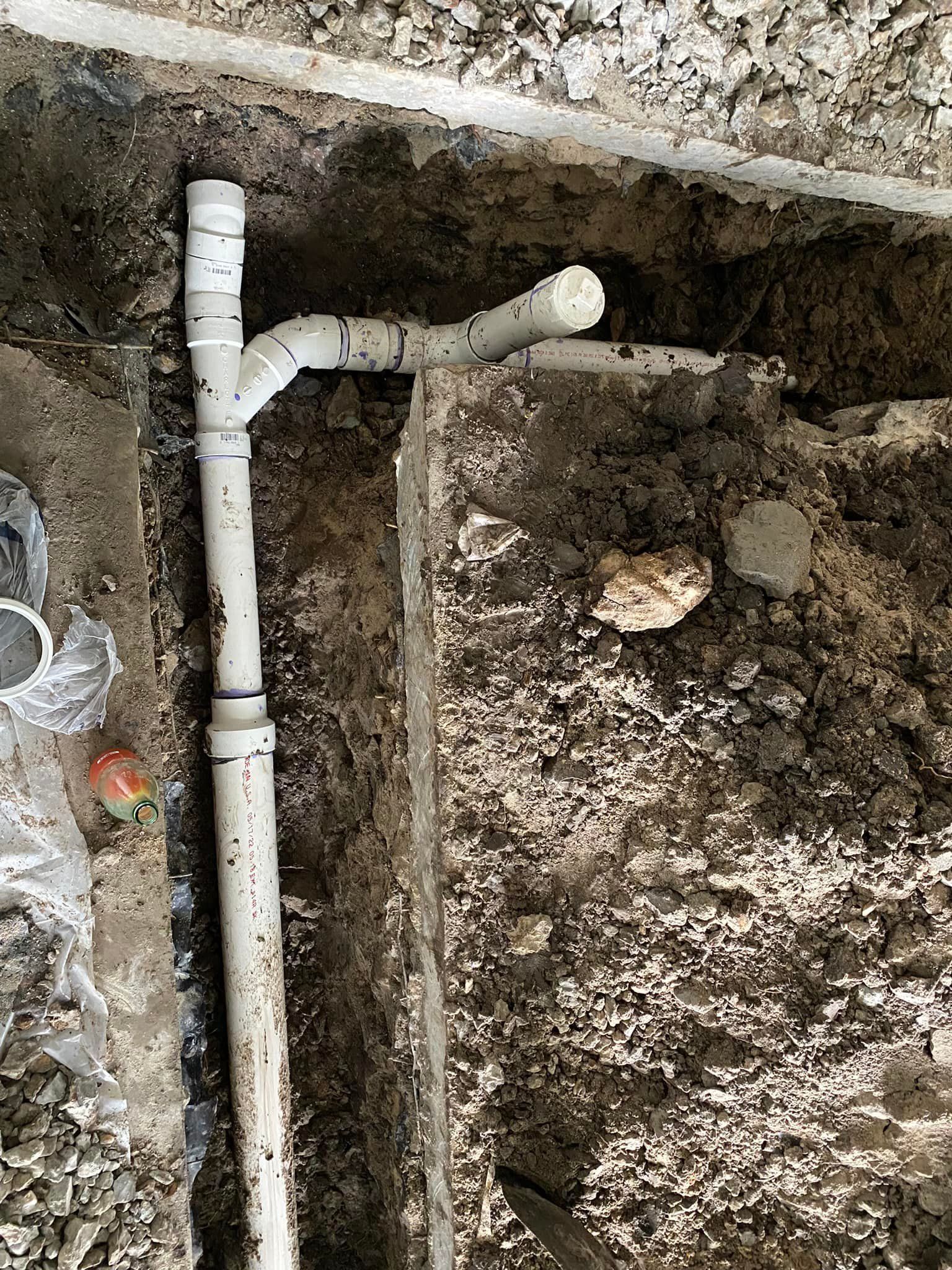 A white pipe is sitting in the dirt next to a wall.