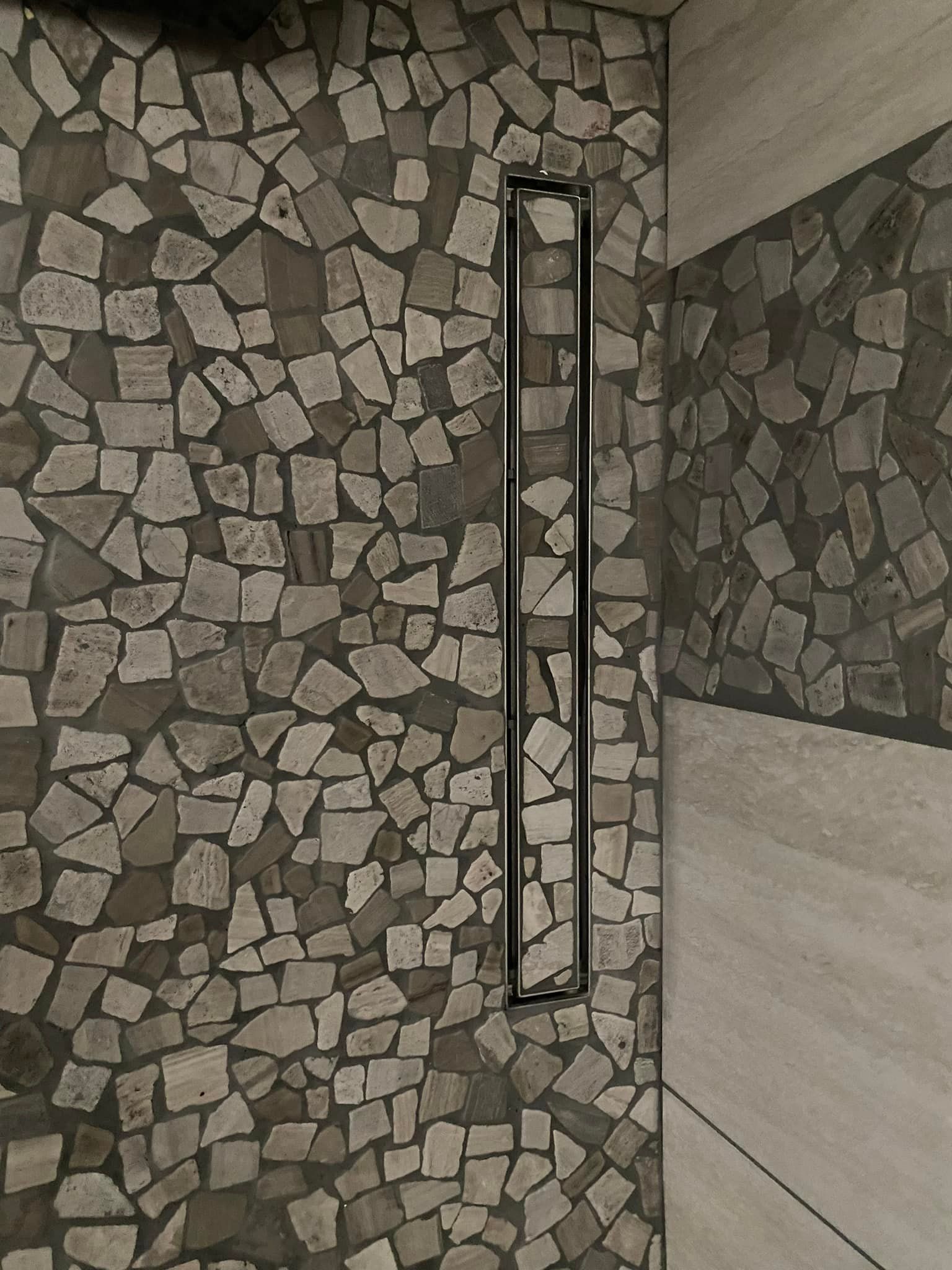 A shower with a stone wall and a drain in the corner.