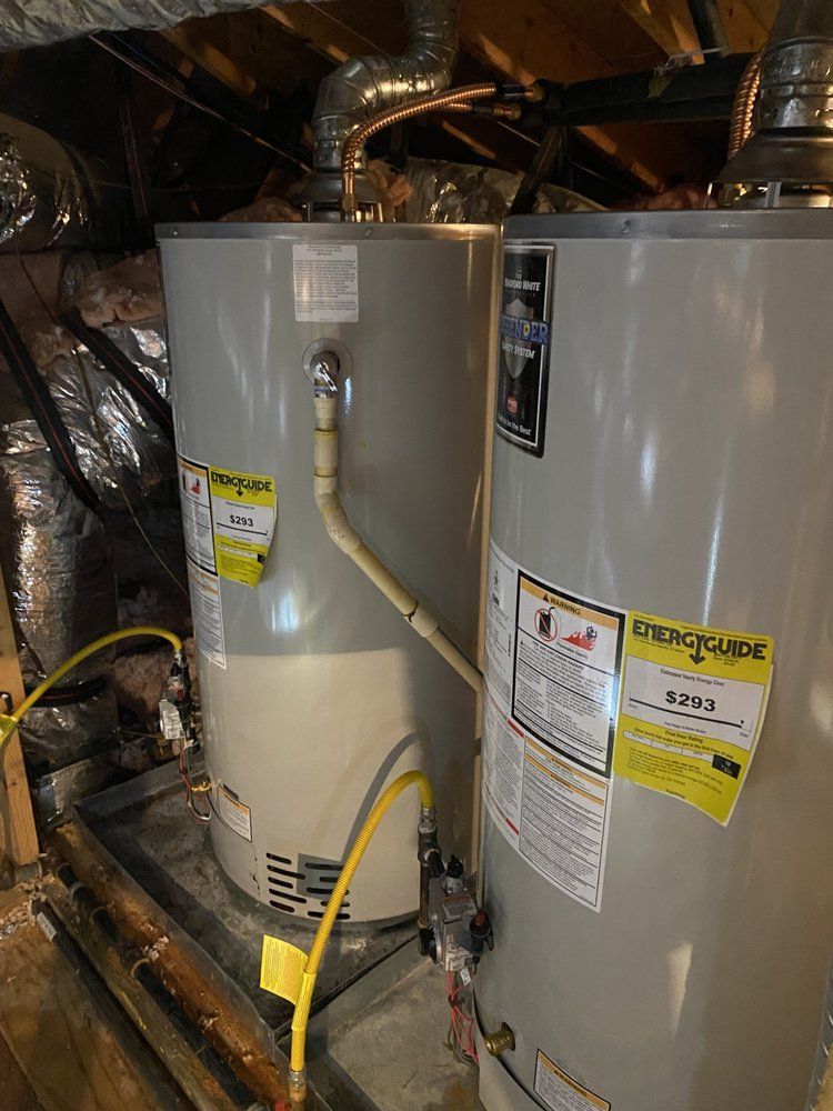 Two water heaters are sitting in the attic of a house.