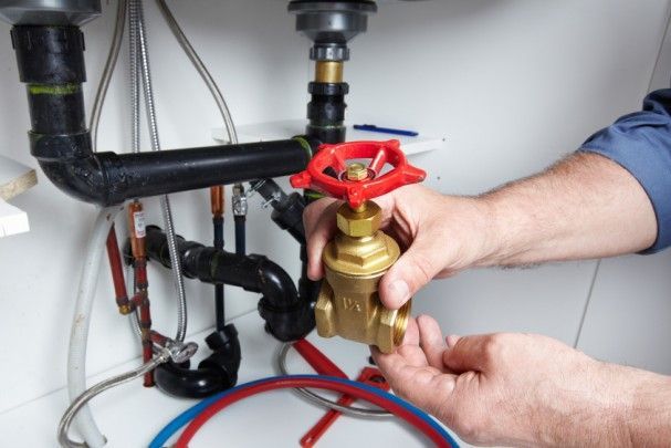 A plumber is fixing a valve under a sink