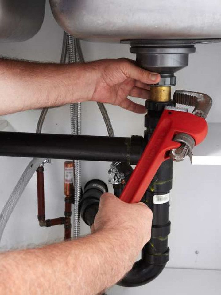 A man is fixing a sink with a wrench