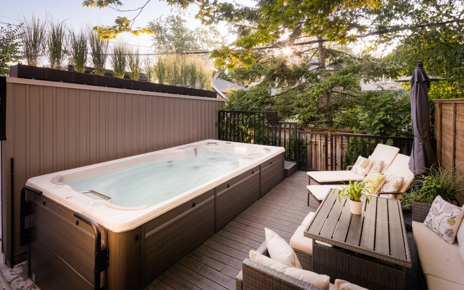 Patio deck with a hot tub, lounge chairs, and potted plants beside a privacy fence