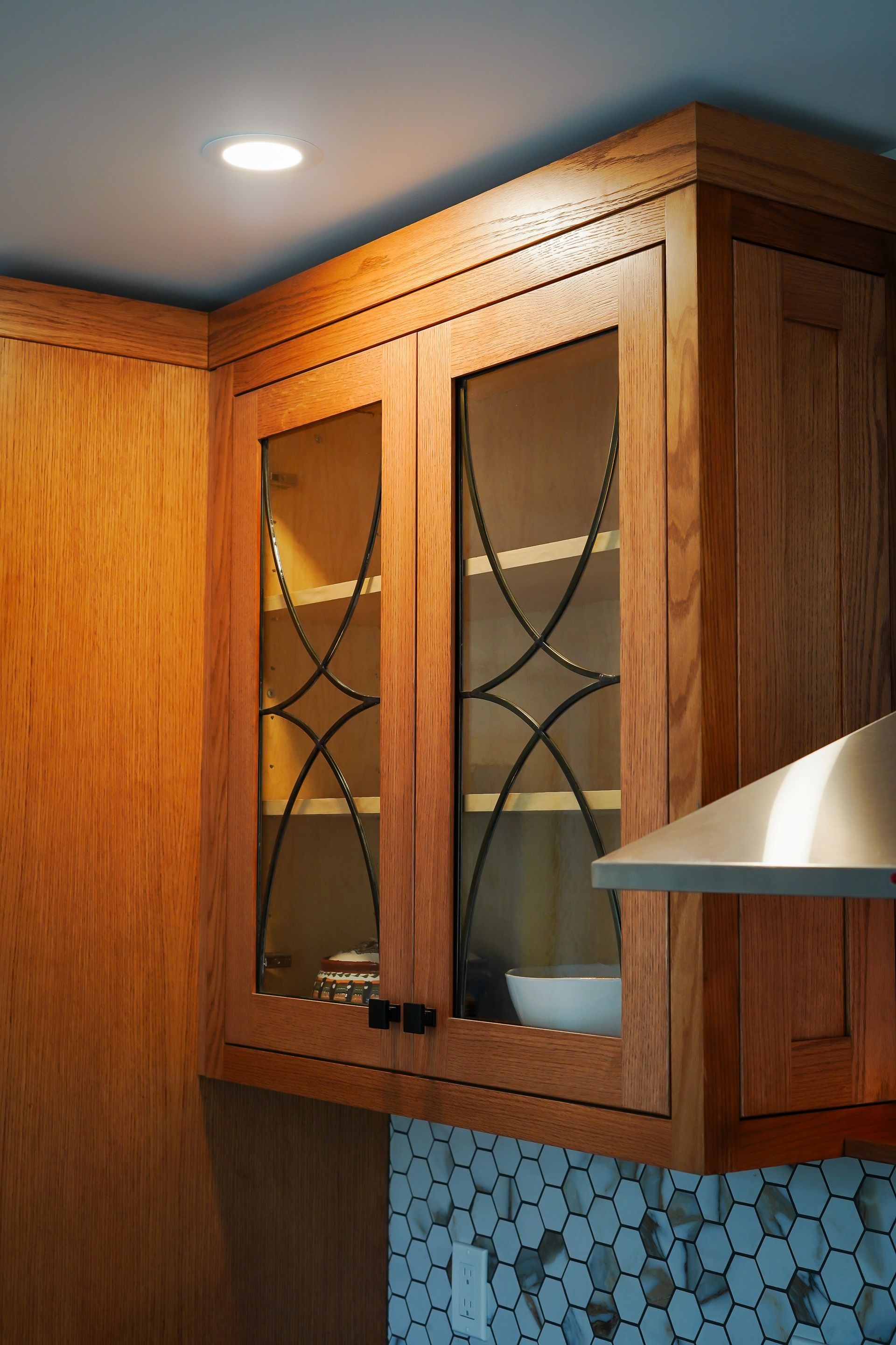 A kitchen with wooden cabinets with glass doors and a stainless steel hood.