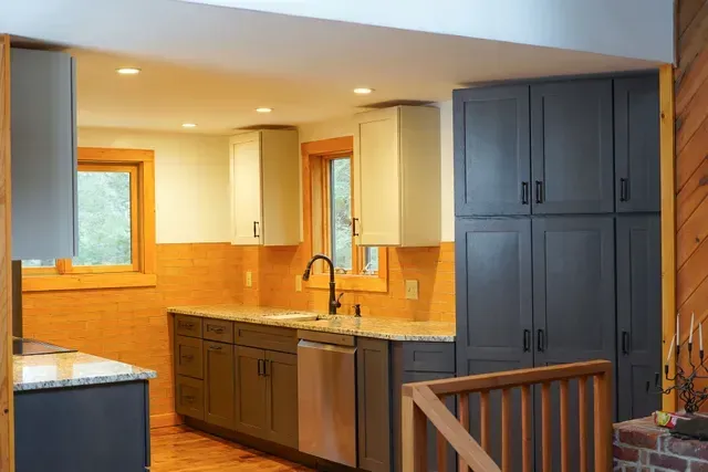 A kitchen with gray cabinets , stainless steel appliances , granite counter tops and a sink.