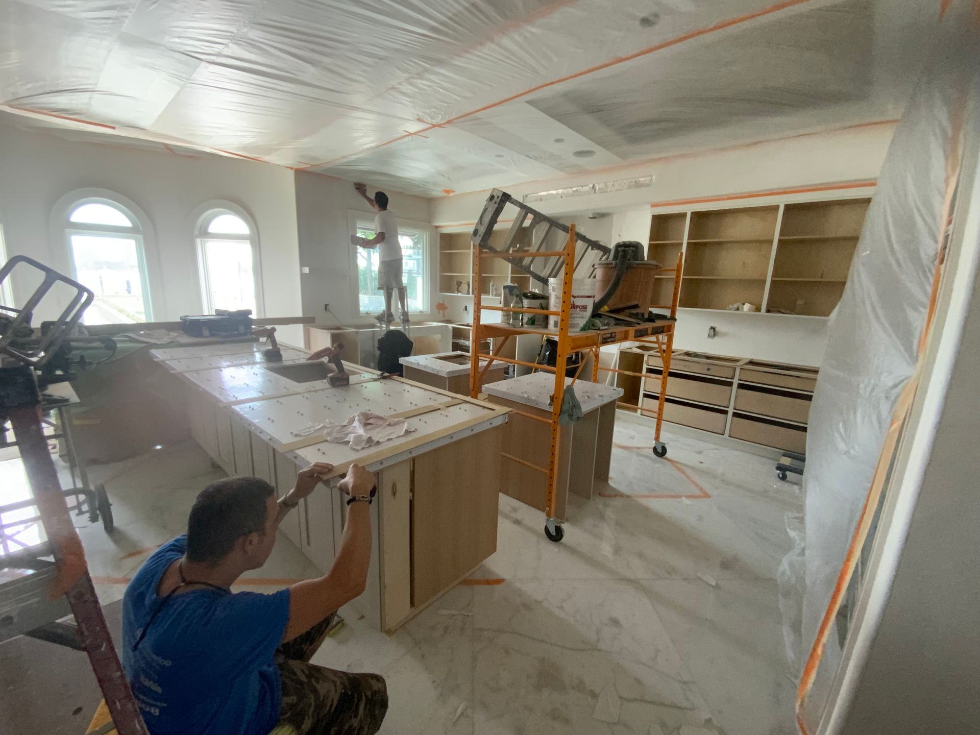 A man is kneeling down in a kitchen painting cabinets.