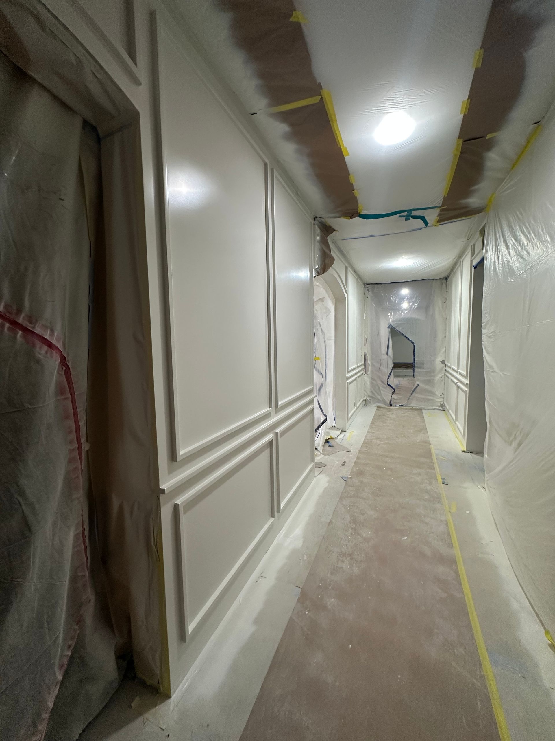 A long hallway with white walls and a staircase in the background.