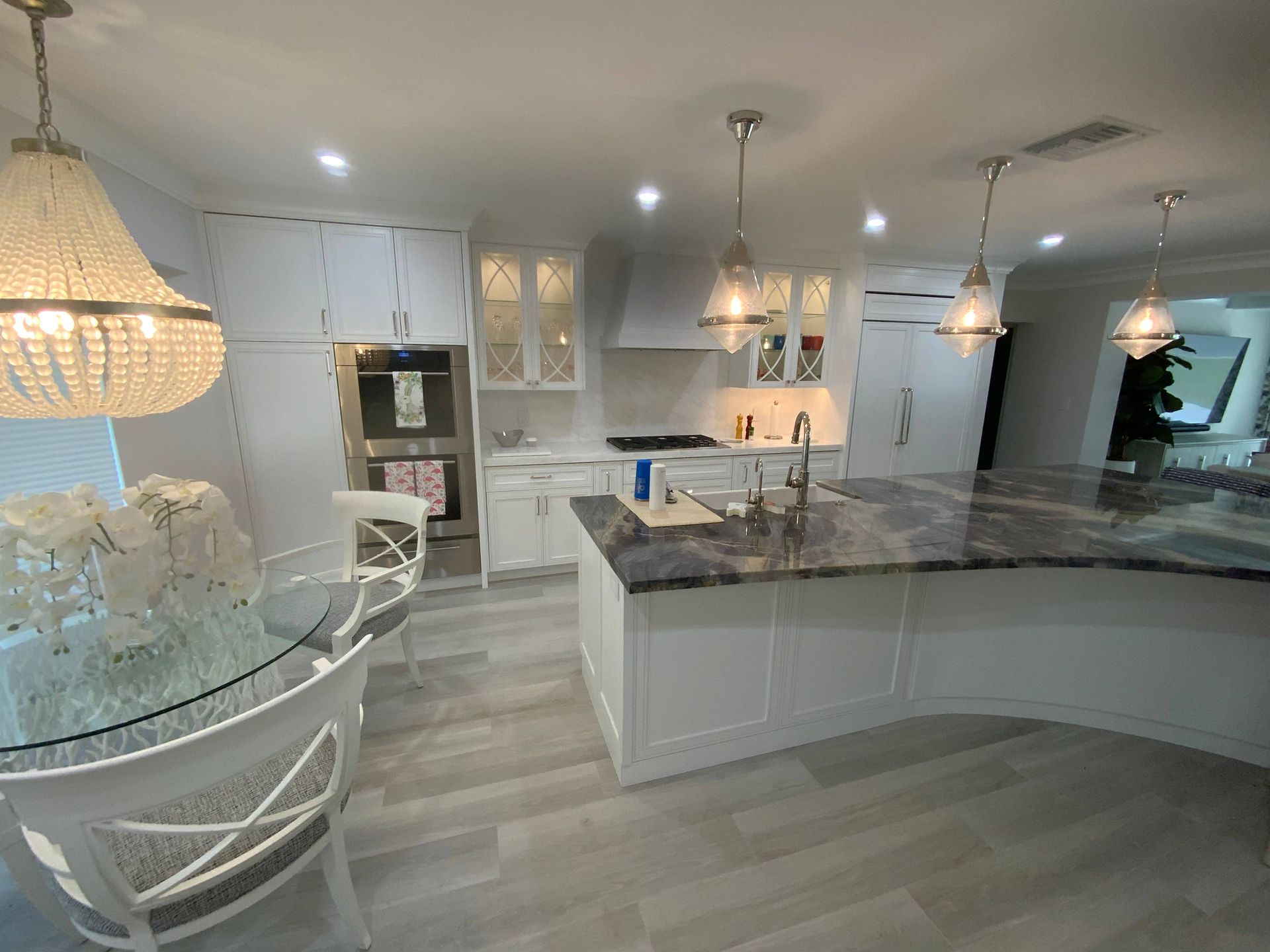 A kitchen with white cabinets , granite counter tops , a dining table and chairs.
