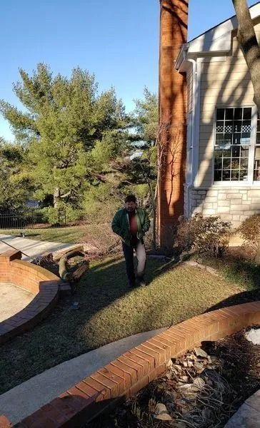Person carrying a white bag on a grassy lawn near a house and tall brick chimney on a sunny day.