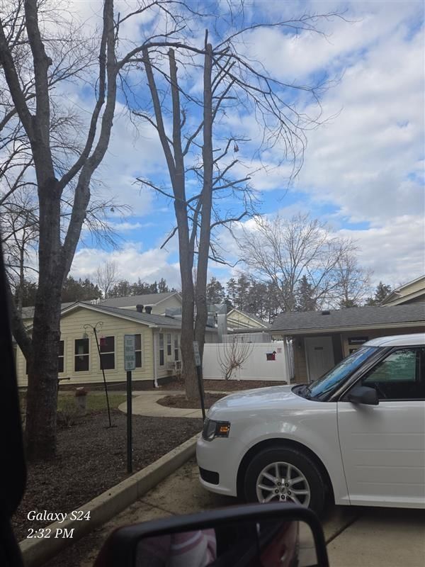 White car parked near a building with bare trees against a cloudy sky.