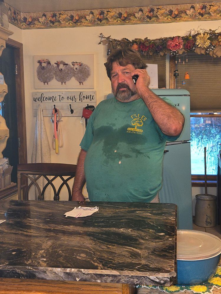 Man on phone in kitchen, wearing green shirt, standing near countertop and refrigerator.