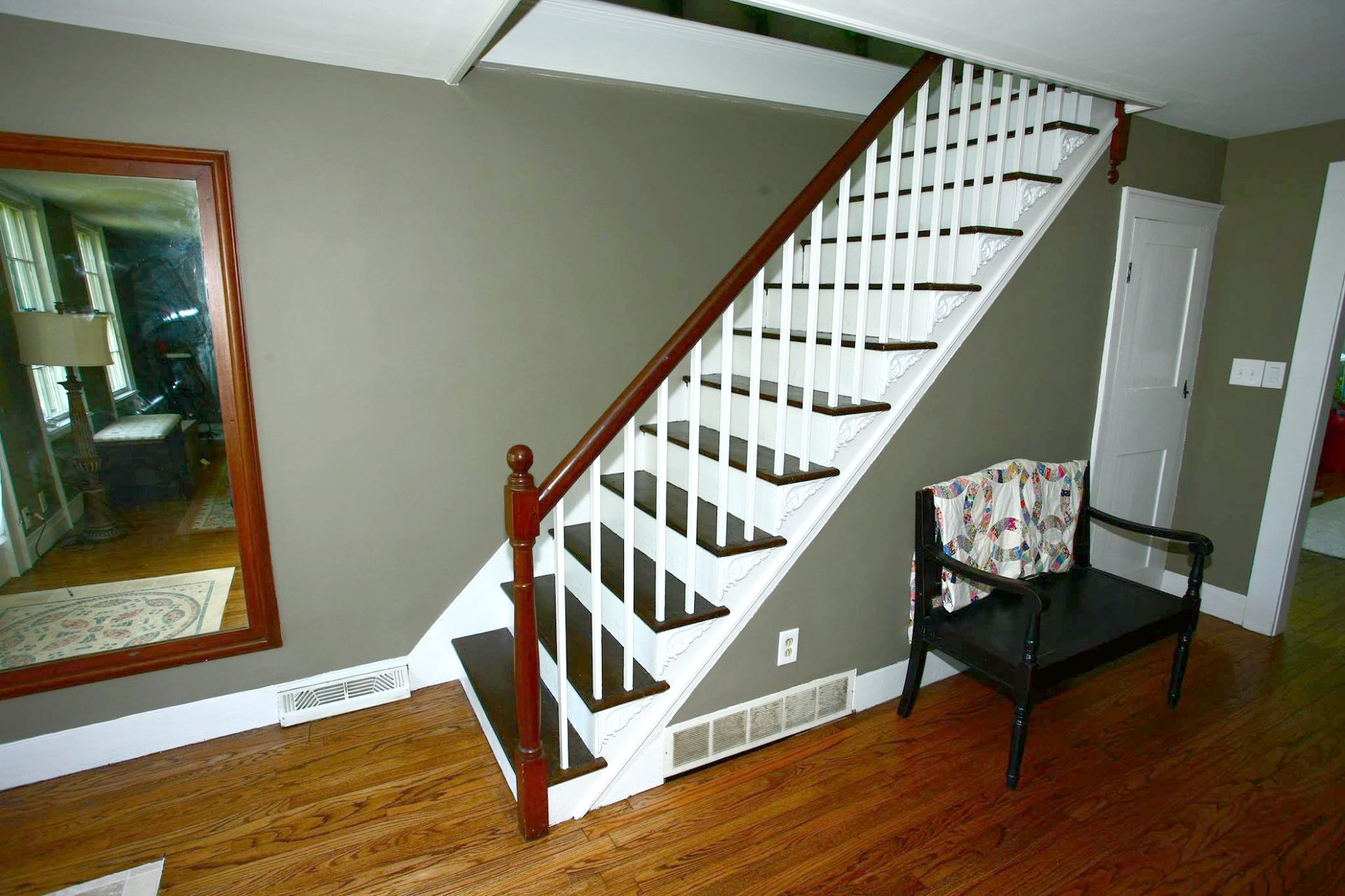 Staircase with white balusters, brown handrail, dark steps, and a bench. Brown hardwood floor and gray walls.