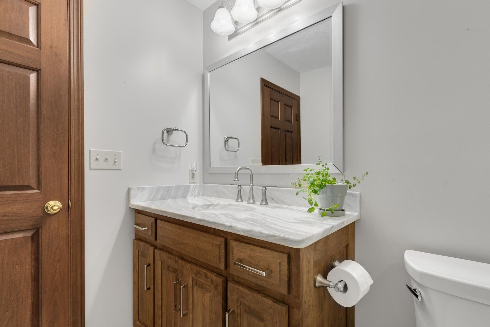 Bathroom with brown cabinet, marble countertop, large mirror, and white toilet.