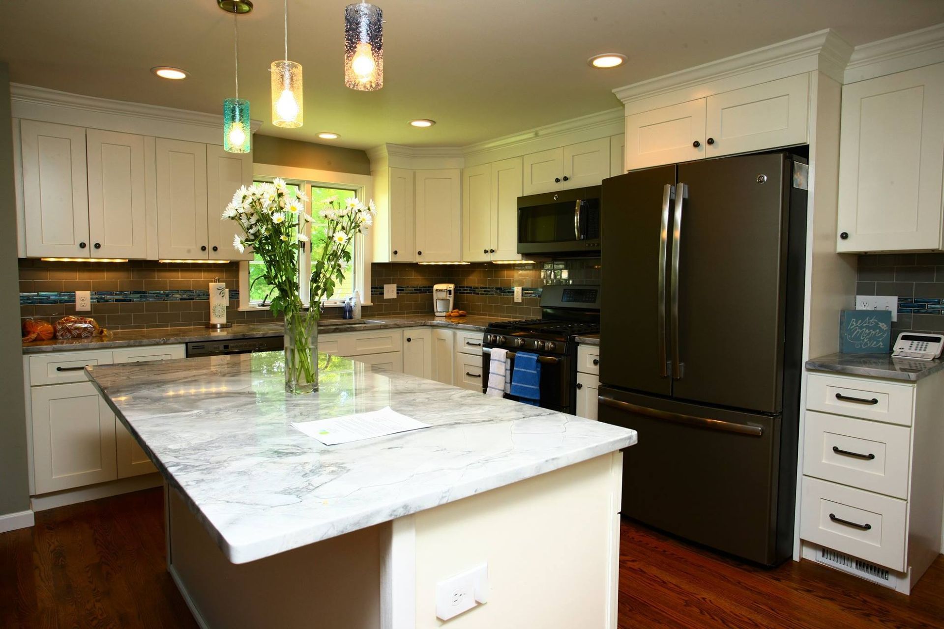 Modern kitchen with white cabinets, dark refrigerator, marble island, and pendant lights.
