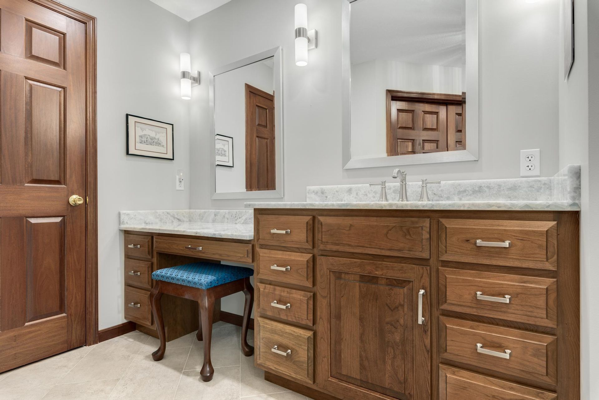 Bathroom with wood vanity, marble countertop, mirrors, and blue vanity stool.