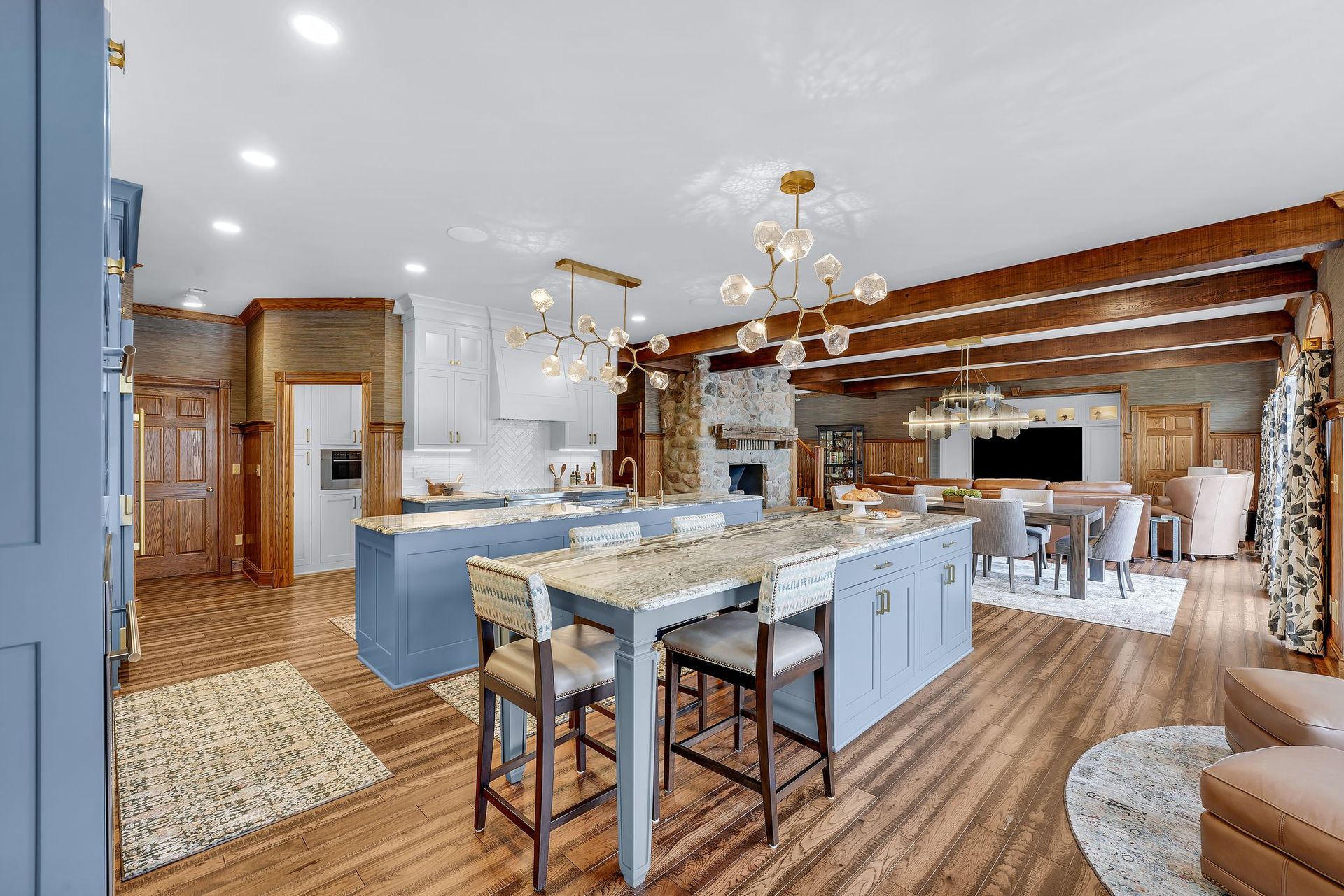 Spacious kitchen with blue island, marble countertops, pendant lights, and wooden beams.